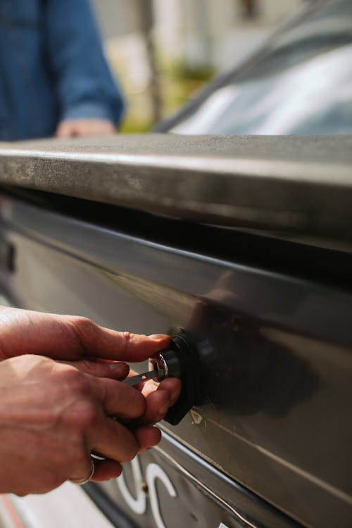 A person using a key to unlock the trunk of a car, representing emergency lockout situations.