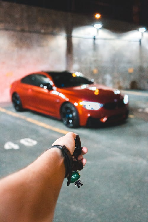 person’s arm holding a key fob directed towards their car, presumably unlocking their car.